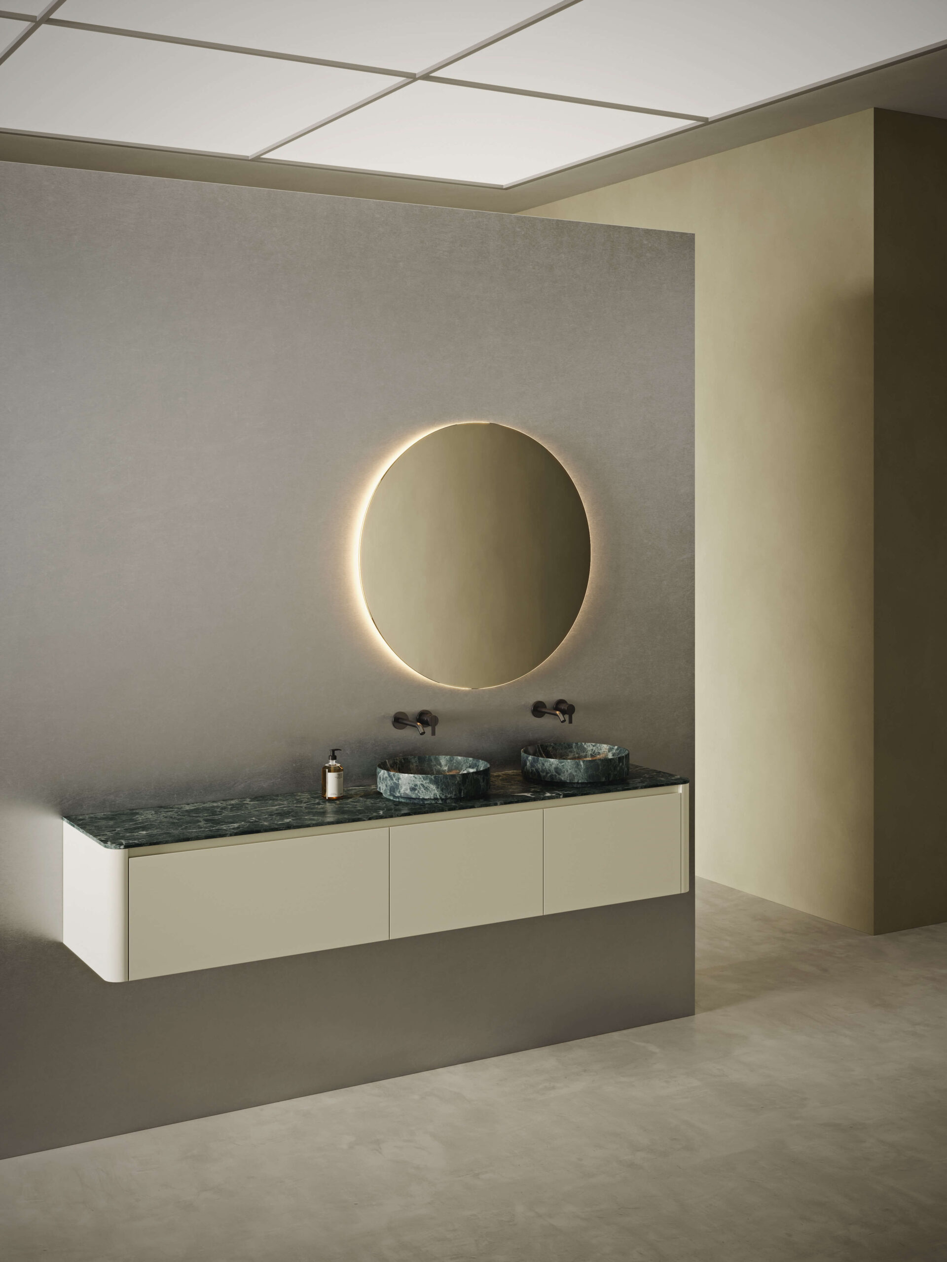 Meuble sous-vasque FUSE à 3 tiroirs, finition laquée brillante Crema 240. Plan de travail simple FUSE de 2 cm et vasque à poser Arc40 en marbre Verde Indalo. Miroir rond STRATO à éclairage LED. Chez Hydropolis