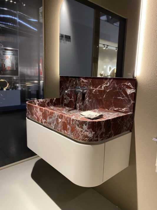 Ella est une réinterprétation du lavabo classique en pierre, où tradition et modernité se rencontrent. Chaque détail a été soigneusement pensé pour une harmonie parfaite entre forme et fonction. Plan de travail avec vasque intégrée en marbre rosso lepanto, meuble haut 1 tiroir.